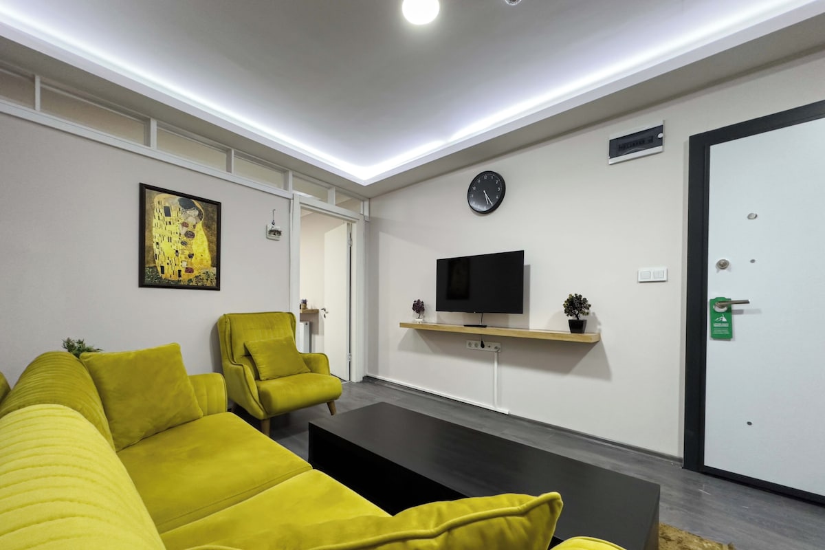 Una sala moderna con un sofá, sillones, un televisor de pantalla plana, un reloj y una puerta.