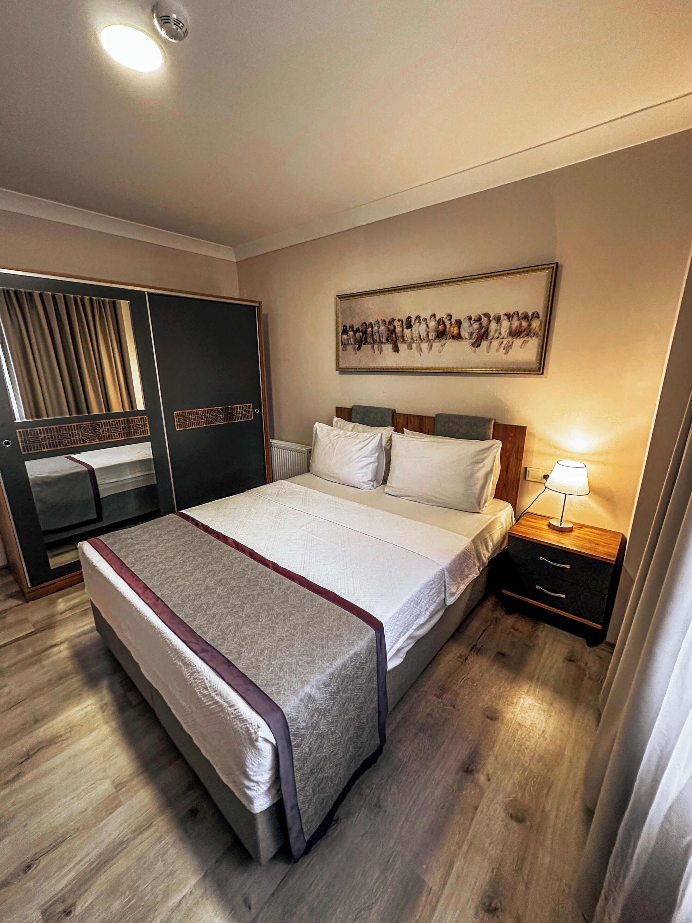 A bedroom with a bed, bedside table, nightstand, wardrobe, and a painting on the wall.