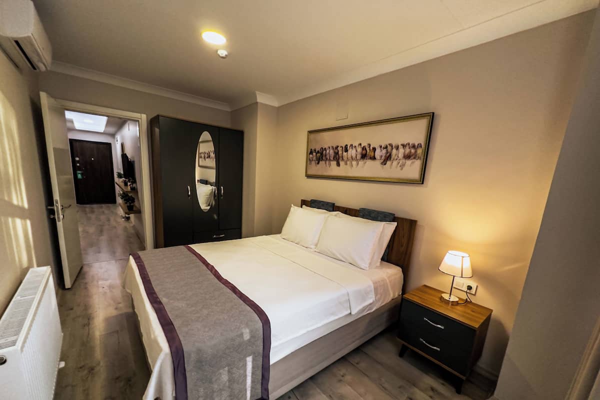 Une chambre d’hôtel comprenant un lit, une table de chevet, une lampe, une armoire et un couloir menant à une autre pièce.