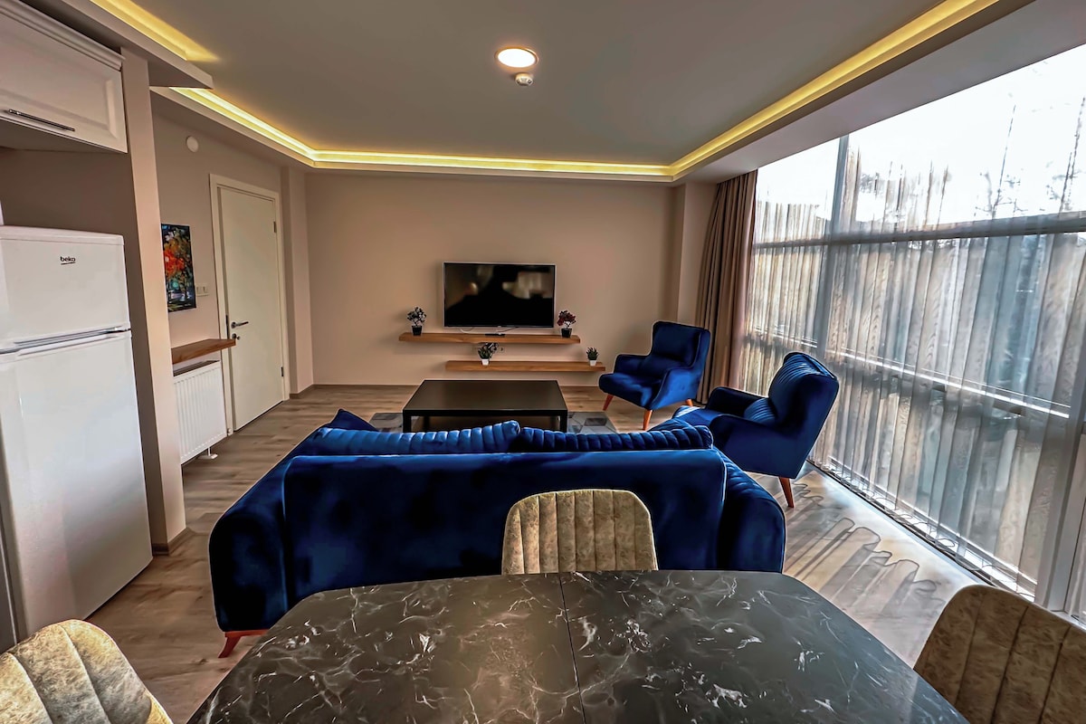 A living room with a sofa set, a TV, a dining table, and a kitchen area with a fridge.
