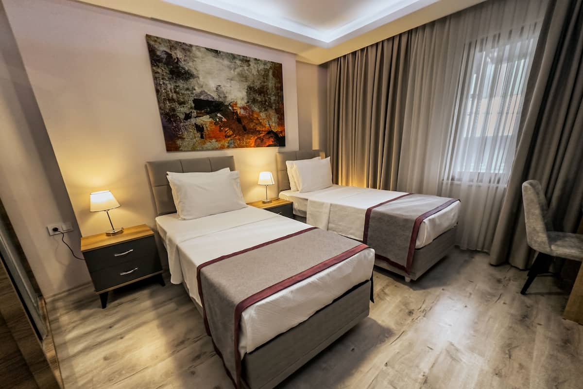 Une chambre d’hôtel avec deux lits, une grande peinture abstraite au mur, une fenêtre avec des rideaux et un plancher en bois.