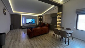 Una sala de estar moderna con un televisor de pantalla plana, un sofá, una mesa de comedor con sillas y un ventanal grande.