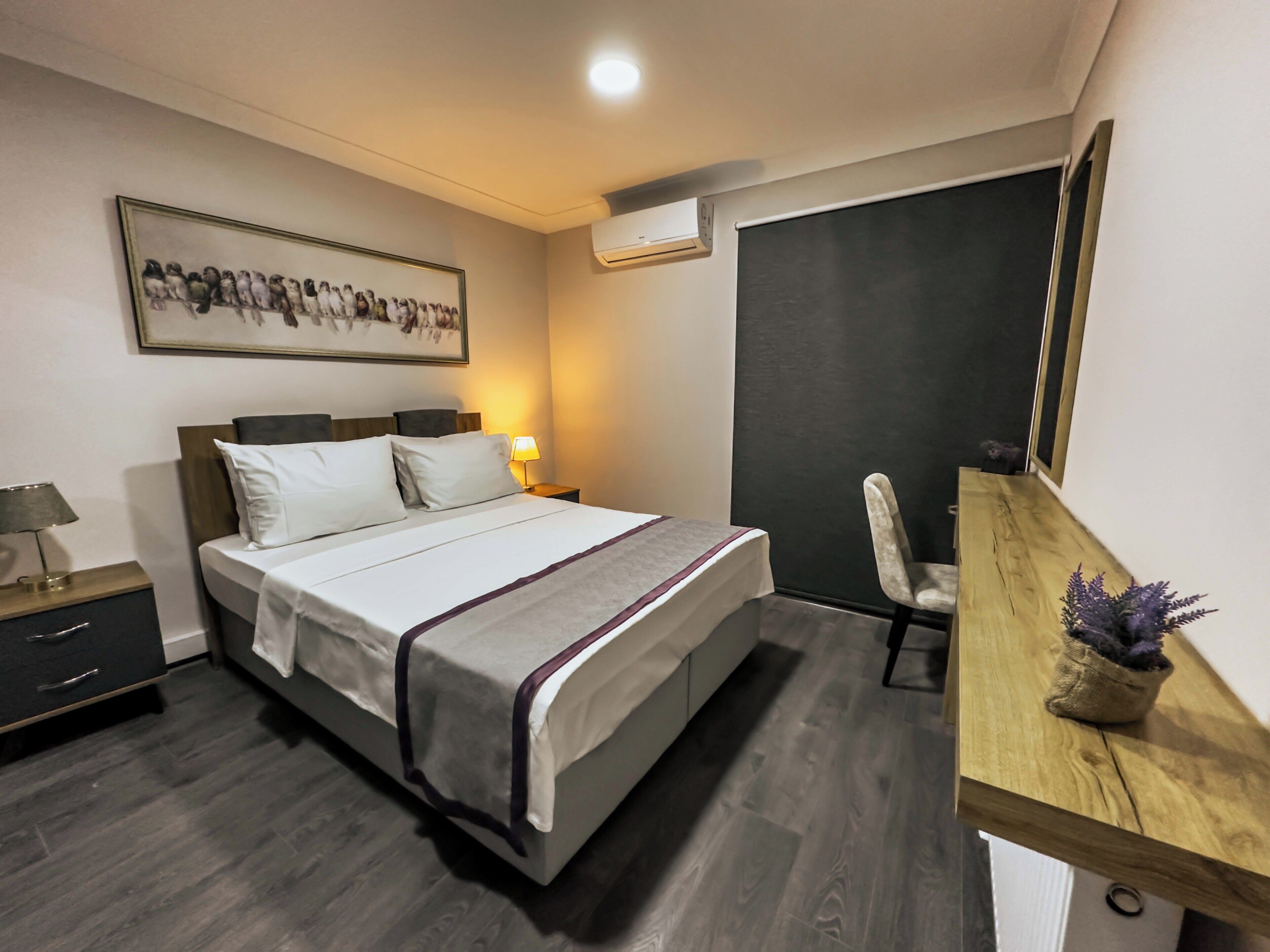A hotel room with a bed, bedside table, lamp, chair, desk, and a framed picture on the wall.