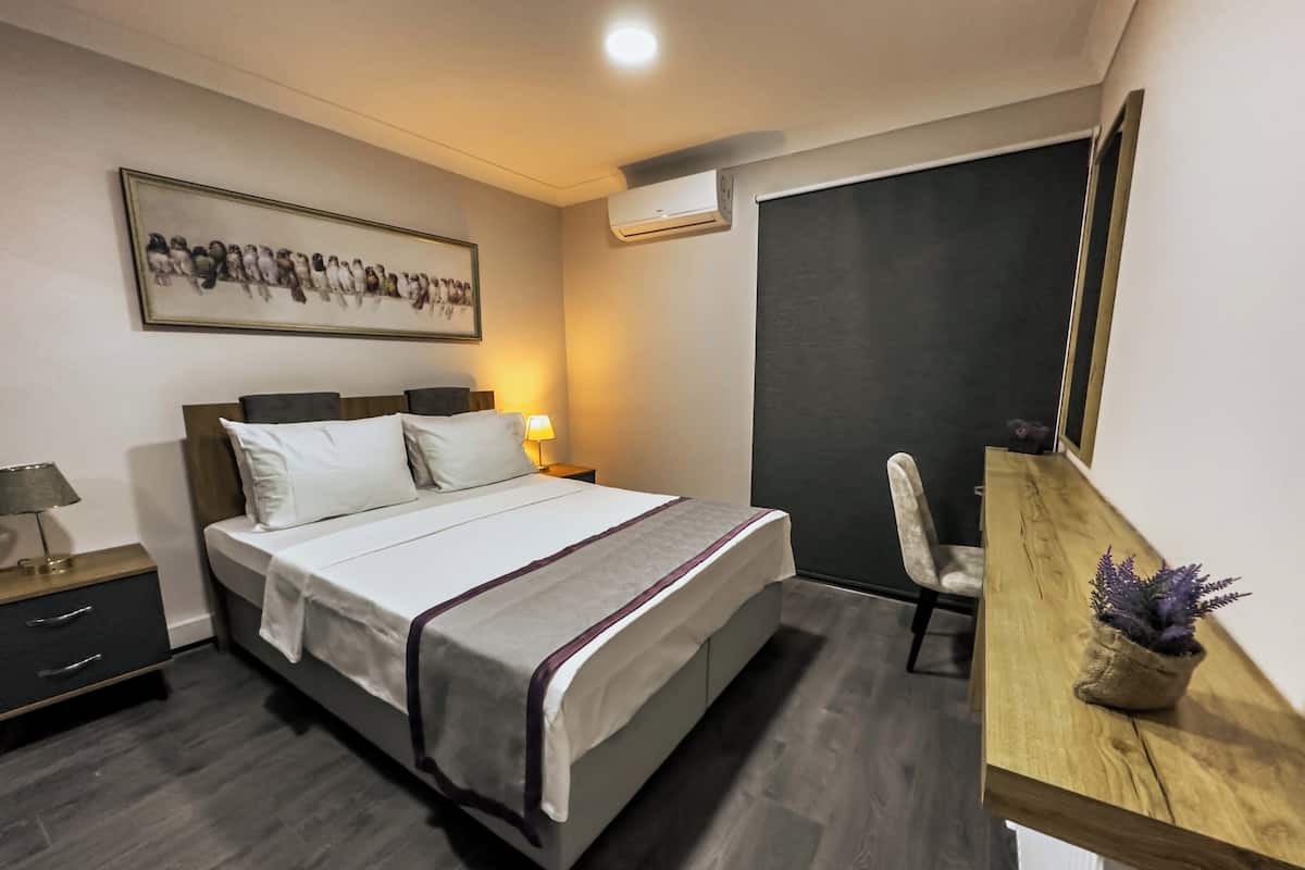 Une chambre d’hôtel comprenant un lit, une table de chevet, une lampe, une chaise, un bureau et un tableau encadré au mur.