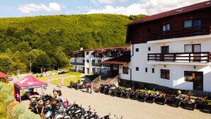 A building with a white facade and a red roof, surrounded by parked motorcycles and a tent. - Hanul Patrisiei (Cartisoara)