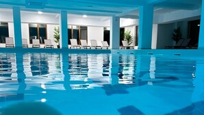 Une grande piscine intérieure à l’eau claire, entourée de chaises longues et de plantes en pot.