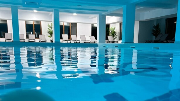 A large indoor swimming pool with clear water, surrounded by lounge chairs and potted plants. - Hanul Patrisiei (Cartisoara)