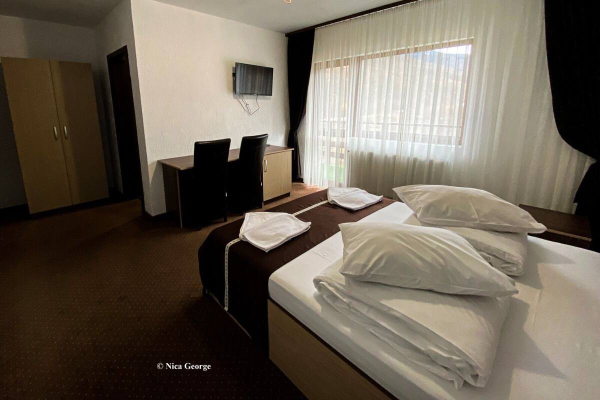 A hotel room with a bed, a desk, a chair, a television, and a wardrobe.