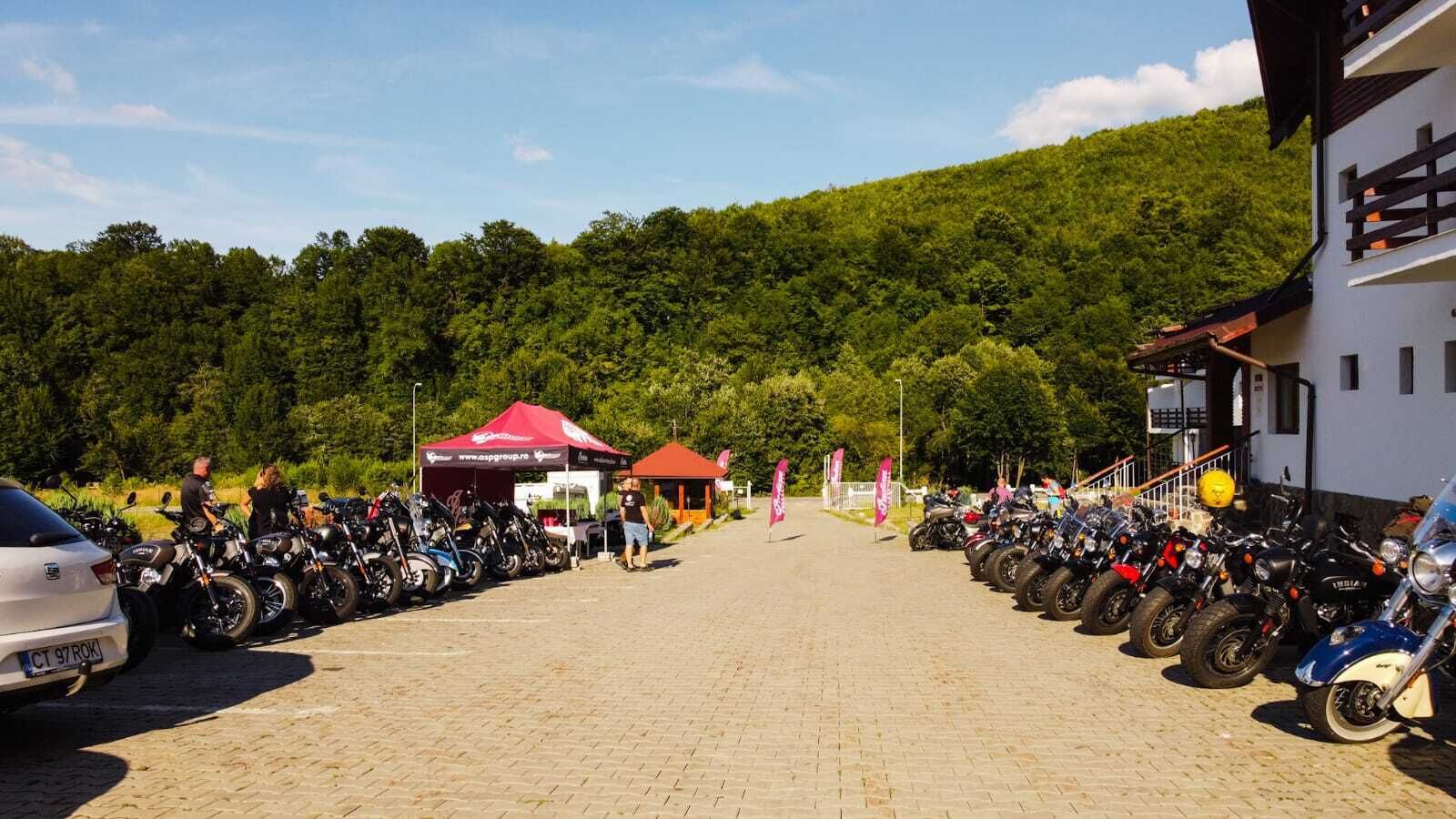 En asfalterad parkeringsplats med motorcyklar uppradade på båda sidor, ett rött tält och en byggnad med en vit fasad.