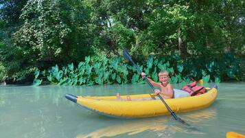 A person in a yellow inflatable raft on a calm river surrounded by lush greenery.