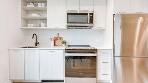 Una cuina moderna amb armaris blancs, un frigorífic d'acer inoxidable, un microones integrat i un forn.
