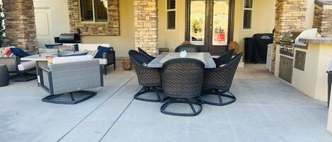 An outdoor patio with stone pillars, a grill, and a dining area with wicker furniture.