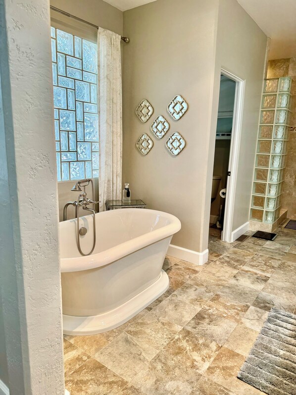 Une salle de bain dotée d’une baignoire sur pieds, d’une douche à parois de verre et de carreaux décoratifs sur les murs.