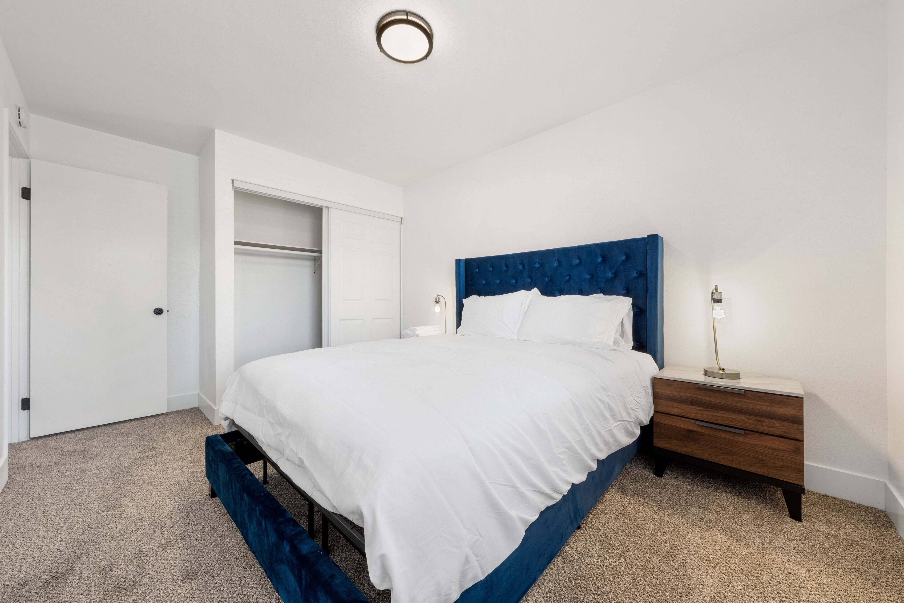 A bedroom with a large bed, a bedside table with a lamp, a wardrobe, and a ceiling light.