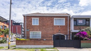Un edificio de ladrillo de dos pisos con una verja de metal negro y un pequeño jardín con flores moradas.