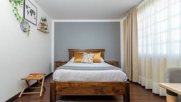 A bedroom with a wooden bed, a small bedside table, a chair, a patterned rug, and a world map on the wall.