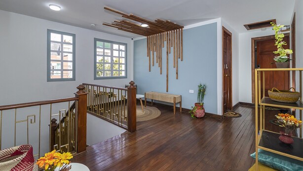 Una habitación amplia con piso de madera, una escalera con barandilla, un banco y un estante con cestas.