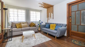 Una sala de estar con un sofá gris, un sofá azul, una mesa de centro blanca y una puerta de madera.