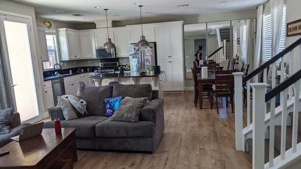A spacious living room with a grey sofa, wooden coffee table, and a dining area with a wooden table and chairs. A kitchen with white cabinets and stainless steel appliances is visible in the background. - Family home at Rohnert Park (Rohnert Park)