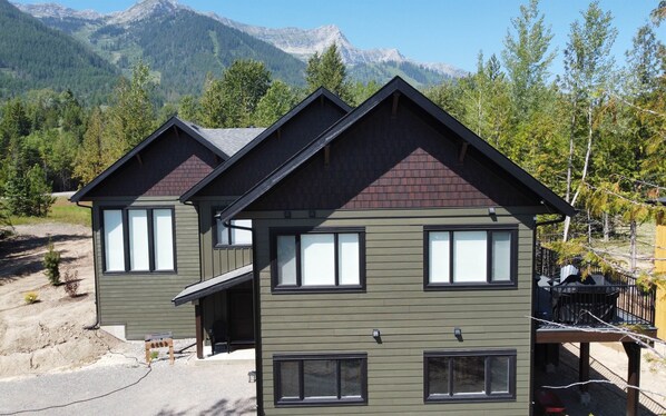 A two-story lodge with a dark green exterior and a red roof, featuring large windows and a balcony with a black railing.