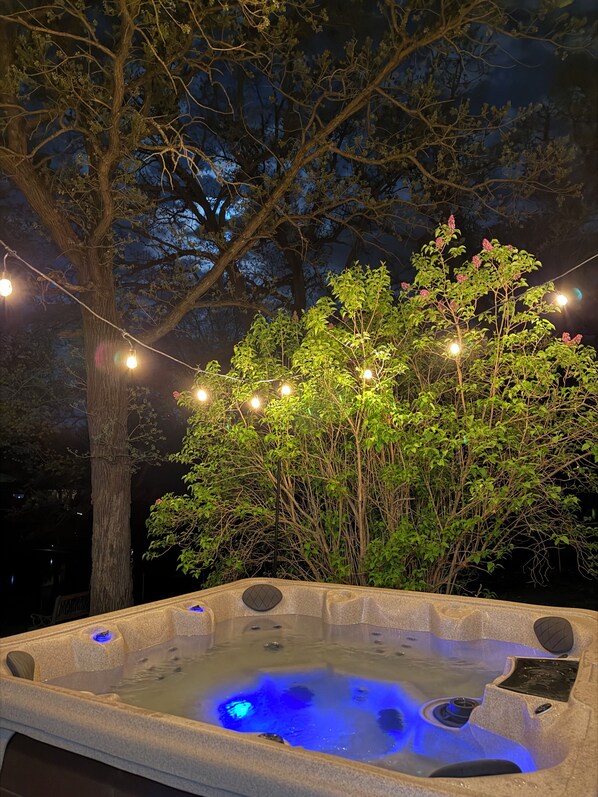 Ein Whirlpool mit Steinfassade, umgeben von Bäumen und Lichterketten.