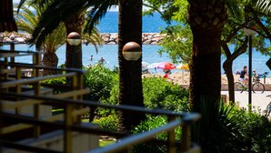 Blick auf einen Strand mit Palmen, feinem Sand und einigen Personen.