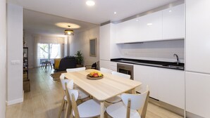 Eine moderne Küche mit weißen Schränken, einem Holztisch mit Stühlen und einer Obstschale.