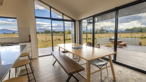 A modern kitchen with large windows, a dining area with a wooden table and benches, and a view of a rural landscape. - Southern Stars - FREE WiFi (Twizel)