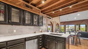A modern kitchen with dark cabinetry, a stainless steel dishwasher, and a large island with a sink. - Lake Travis Gem, Golf, boat, Tennis, Pool (Point Venture)