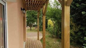 Ett trädäck med en pergola, som leder vidare till en trädgårdsdel med träd och grönska.