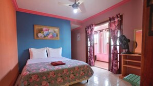 A bedroom with a bed, a ceiling fan, a window with curtains, and a small table. - Suíte Palmeiras  (Cabo Frio)