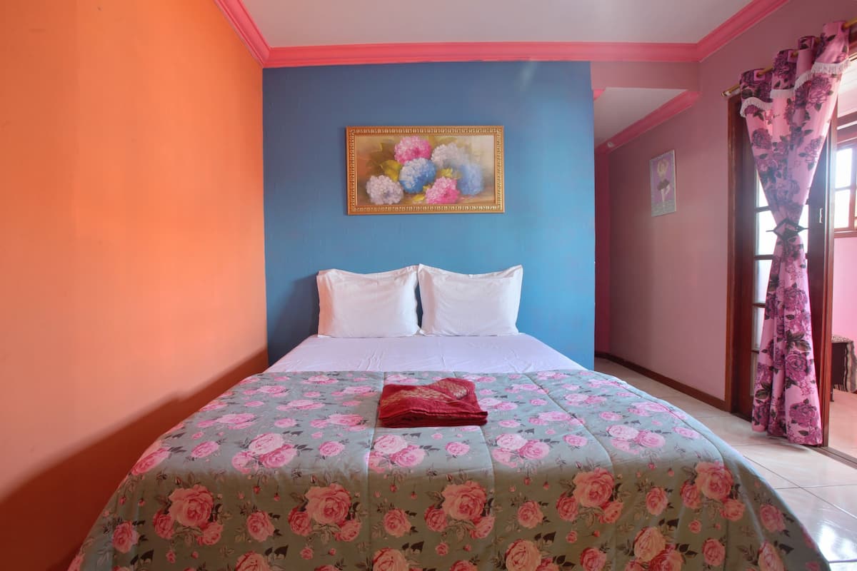 A bed with a floral bedspread, a painting on the wall, and a window with curtains.