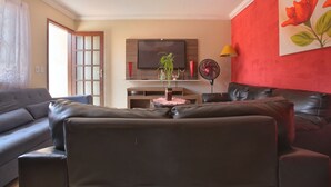 A living room with a sofa, a TV, a plant, and a red wall. - Suíte Palmeiras  (Cabo Frio)