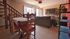 A living room with a dining table, chairs, a sofa, a television, and a staircase. - Suíte Palmeiras  (Cabo Frio)