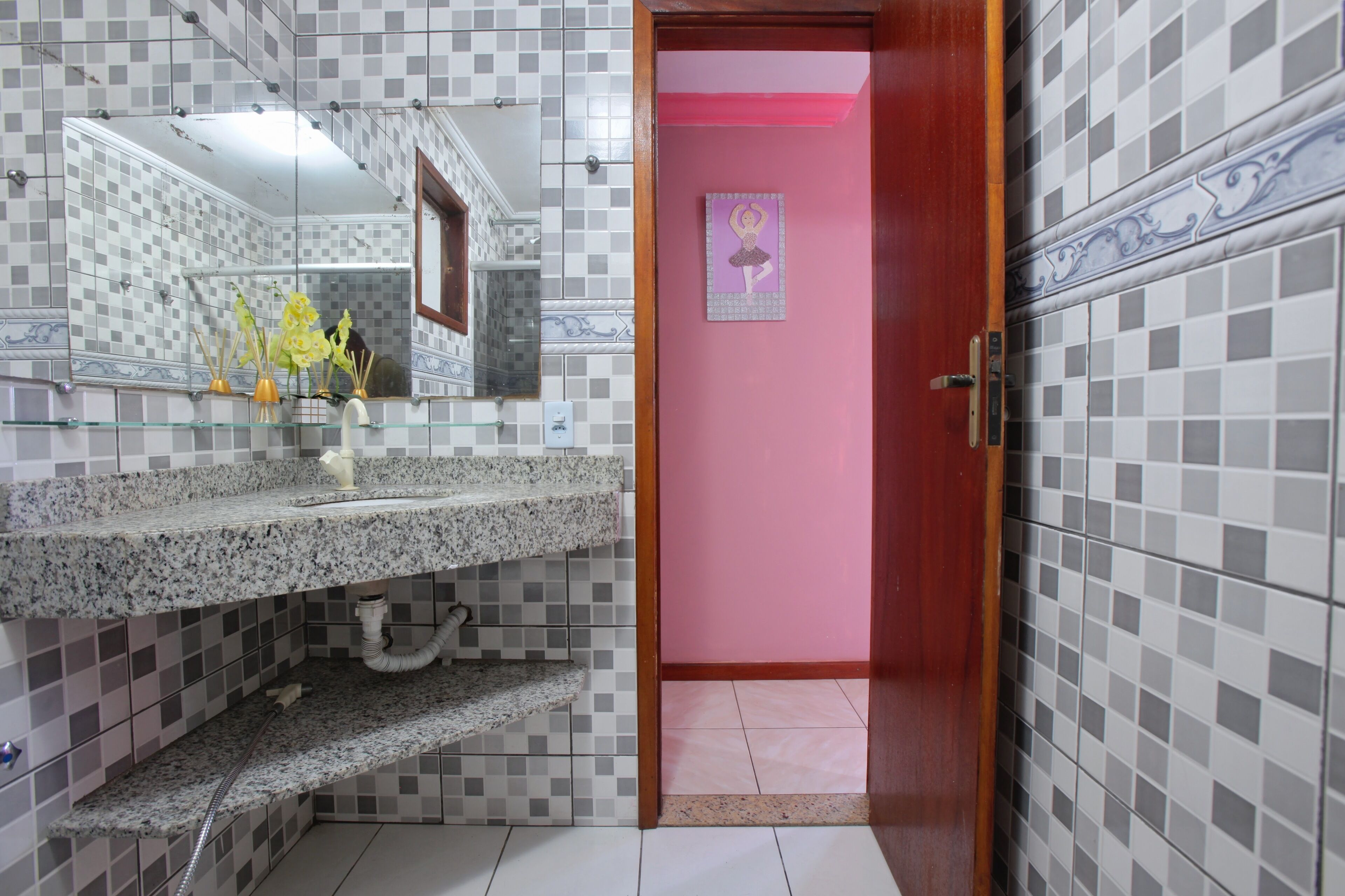 A bathroom with a tiled wall, a mirror, a sink with a granite countertop, and a pink door.