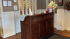 A reception desk with a wooden finish, a vase with flowers, and framed certificates on the wall. - Publick House Hotel Inc. (Chester)