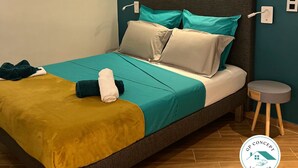 A modern bedroom with a bed, teal and beige bedding, a small bedside table, and a wall-mounted light fixture. - Renovated 37m2 studio located 30 meters from Anse à L'âne beach (TROIS ILETS)