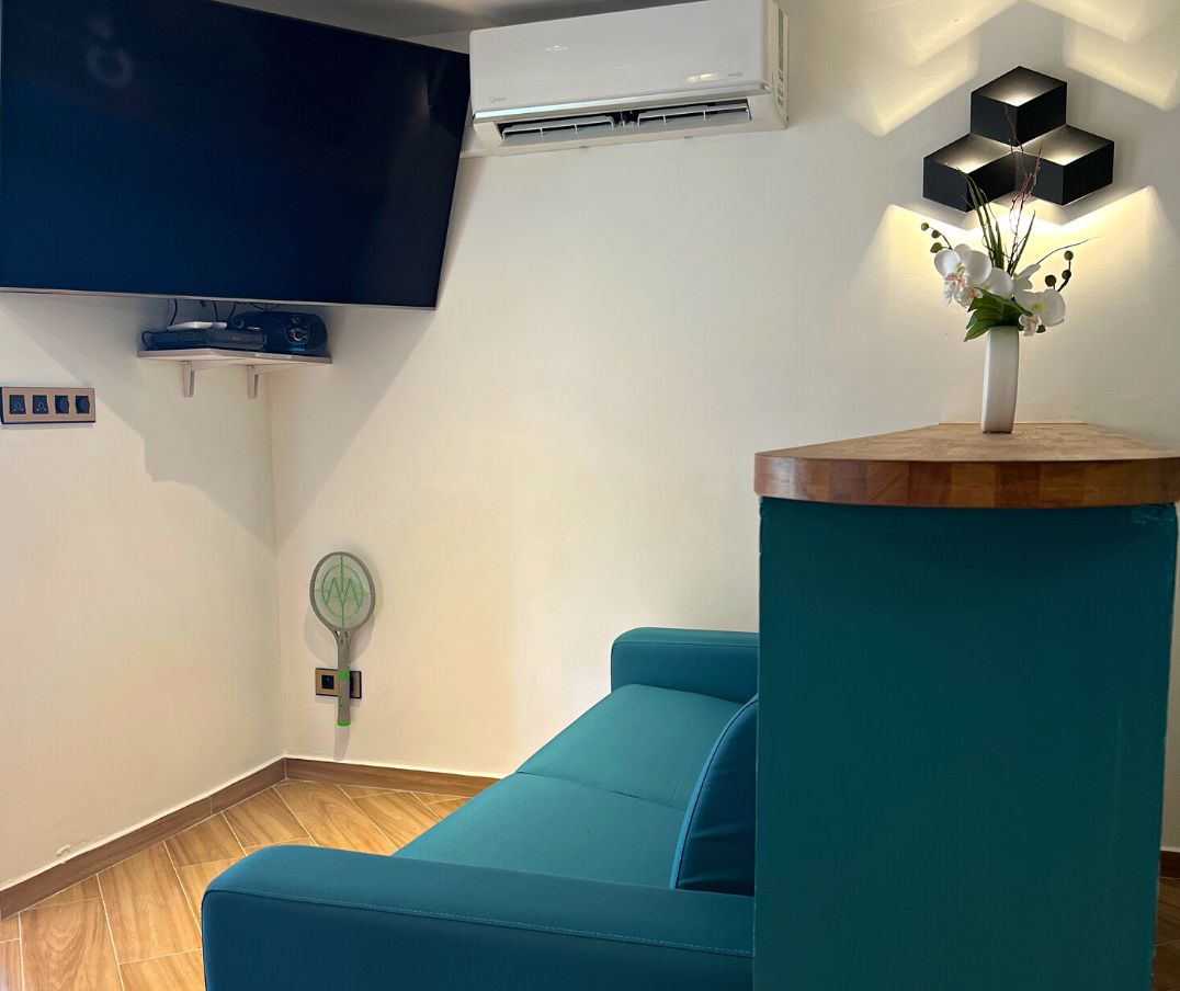 Un sofá color turquesa, un televisor de pantalla plana, un aire acondicionado, un adorno en la pared y un logotipo en un pilar color turquesa.