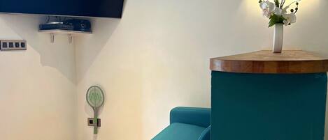 Un sofá color turquesa, un televisor de pantalla plana, un aire acondicionado, un adorno en la pared y un logotipo en un pilar color turquesa.