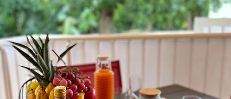 A table with a fruit bowl, a bottle of sauce, and a basket of pastries on an outdoor patio.