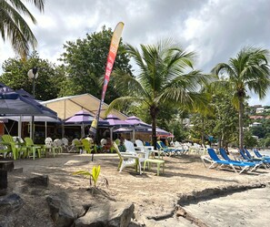 Ubicación frente a la playa con sillas de descanso, sombrillas y un cartel que dice 'Hard Cider'.