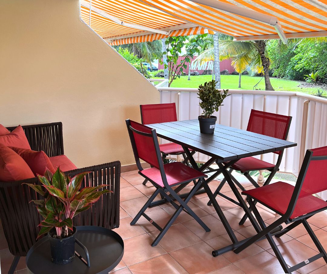 Een terras buiten met een tafel, stoelen, een bloempot en uitzicht op een tuin.