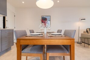 A modern dining area with a wooden table set for four, grey upholstered chairs, and a vase with red foliage on the table. - Tabas | Moderno apto em Ipanema - RJ | IP0019 (Rio de Janeiro)