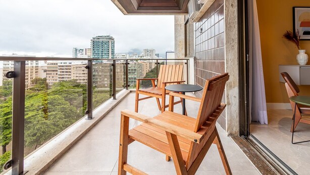 A balcony with wooden furniture, a city view, and a tiled wall. - Tabas | Moderno apto em Ipanema - RJ | IP0019 (Rio de Janeiro)