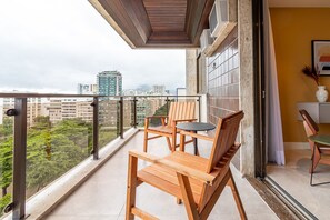 A balcony with wooden furniture, a city view, and a tiled wall. - Tabas | Moderno apto em Ipanema - RJ | IP0019 (Rio de Janeiro)