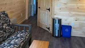 Ein Holzblock-Interieur mit einer Couch, einem an der Wand montierten Fernseher und einem Deckenventilator.