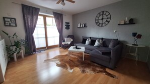 A modern living room with a grey sofa, a white coffee table, a leather rug, and a large wall clock. - Vacation apartment "Bergliebe"  (Germaringen)