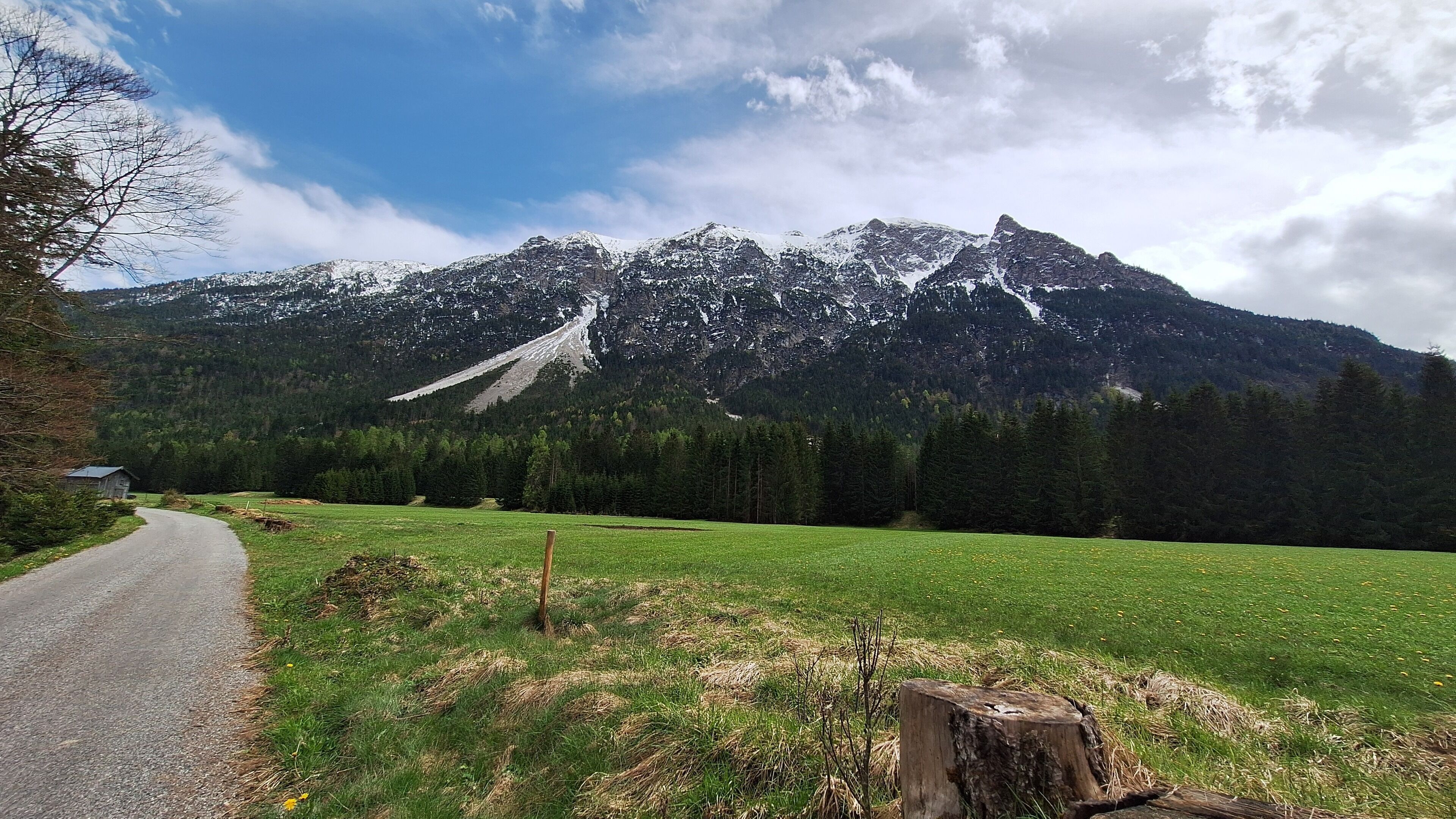 A rural road leading to a mountain range with a small building on the left.
