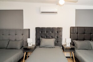 A modern hotel room with a large bed, two bedside tables, and an air conditioning unit.
