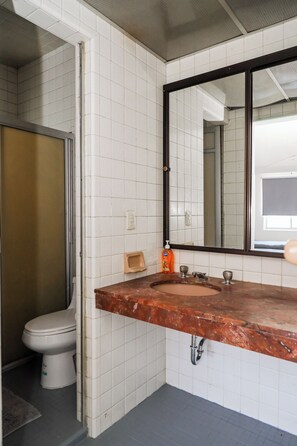 A bathroom with white tiled walls, a marble sink, a toilet, and a mirror.